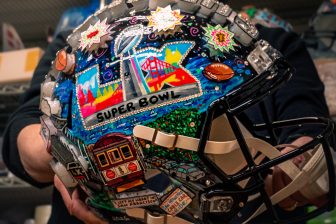 Charles Fazzino holds the Super Bowl LX helmet out in front of him to show all the 3D pop art details