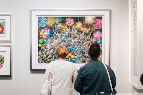 Two gallery attendees look at artwork on the wall that is brimming with fireworks and iconic landmarks across the globe