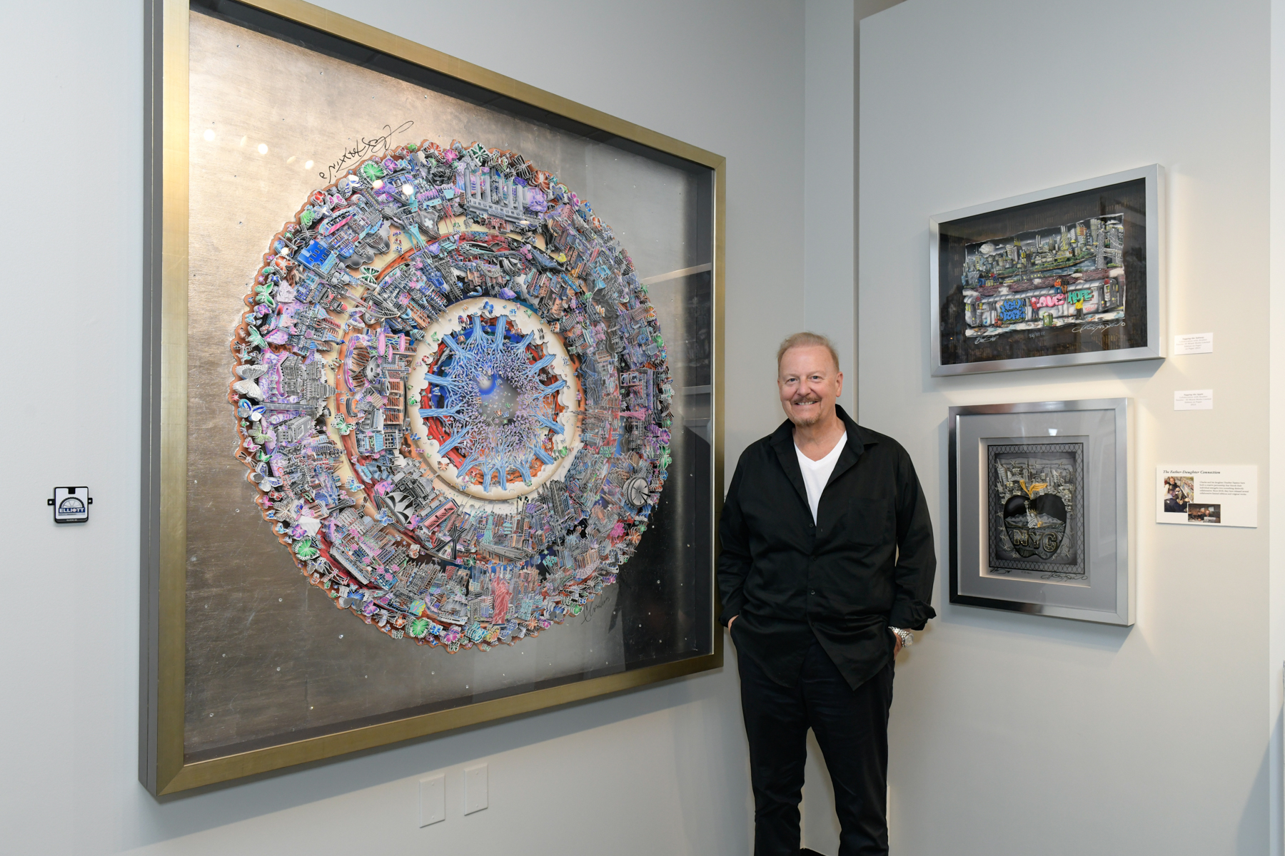 Charles stands smiling in front of one of his iconic world pieces shown at the Elliot Museum