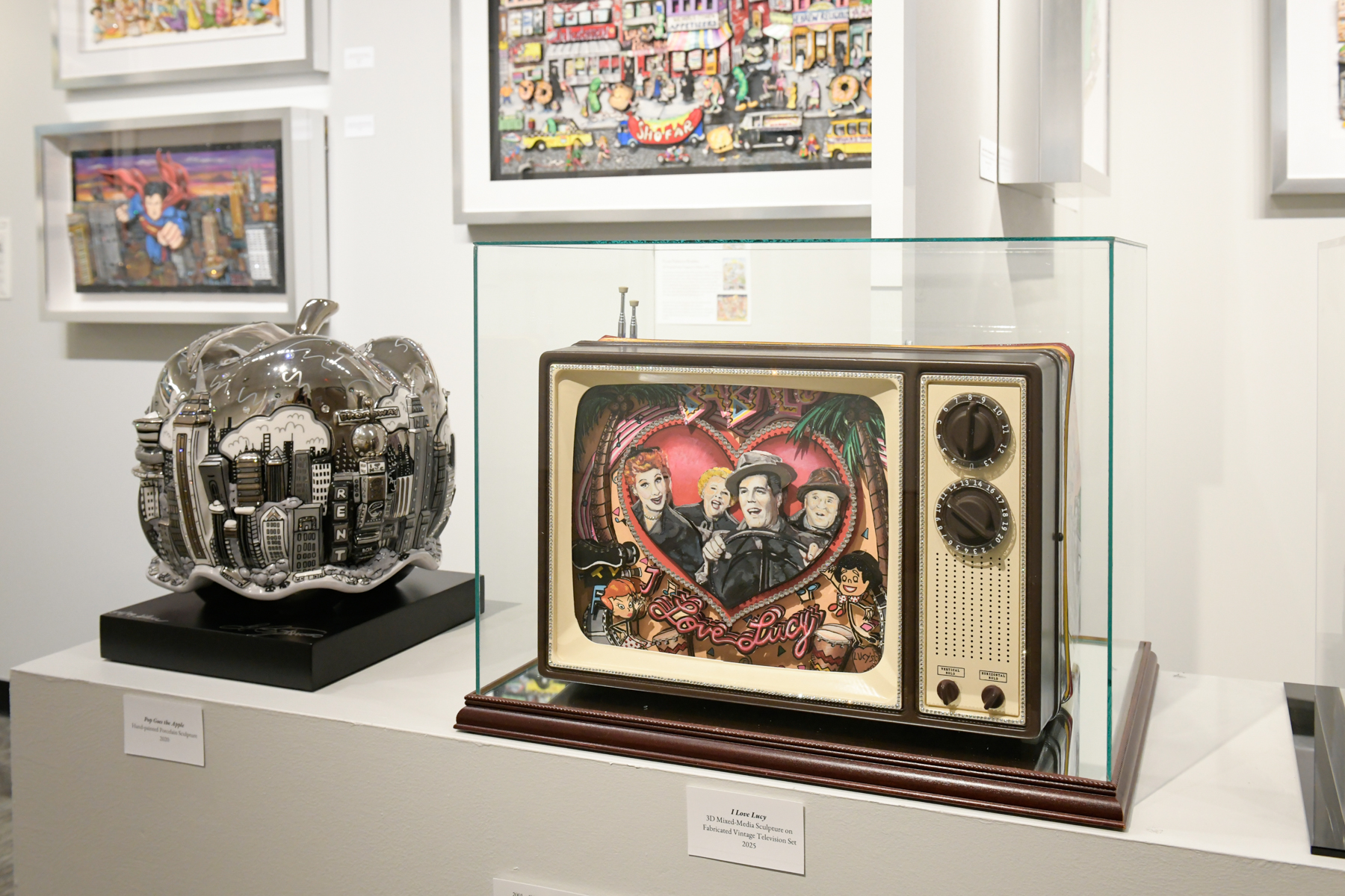 A display case features one of Fazzino's TV's with characters from I Love Lucy and a big apple sits next to it covered in iconic landmarks in NYC